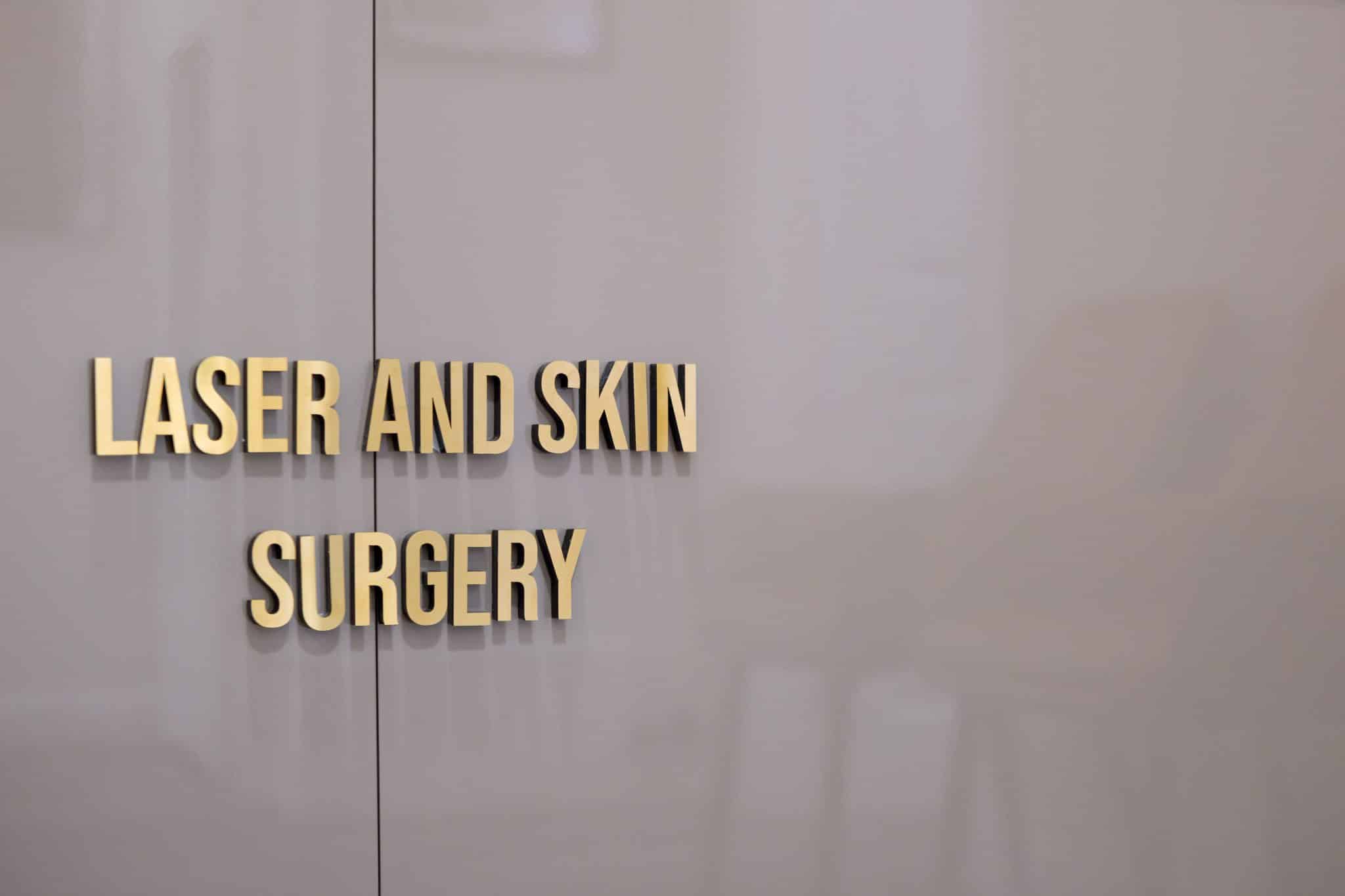 Sign on a gray wall reading 'LASER AND SKIN SURGERY' in gold letters.