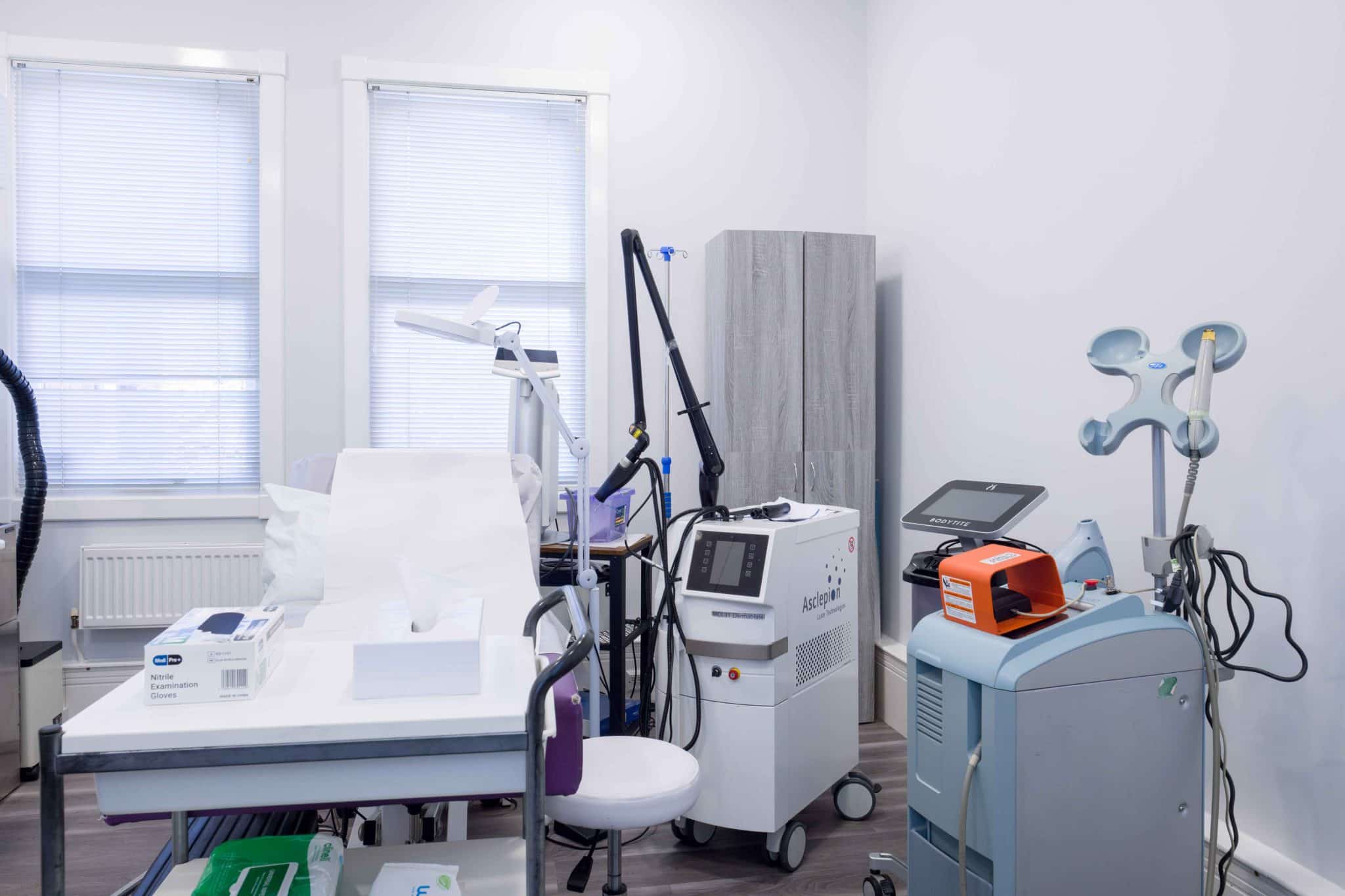 Clinical laboratory workspace with multiple medical devices, a tissue box, and gloves on a counter near large windows with blinds